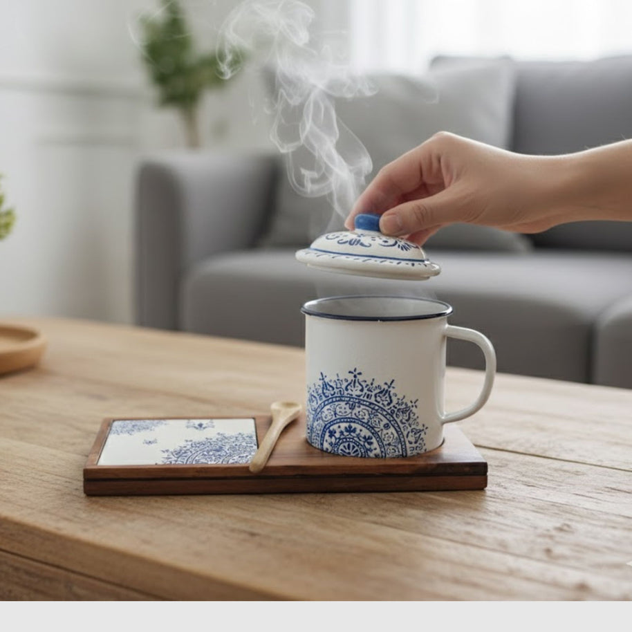 Hand lifting the lid of a steaming Senja Indigo batik mug on its wooden tray with coaster, styled in a living room