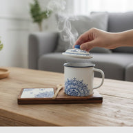 Hand lifting the lid of a steaming Senja Indigo batik mug on its wooden tray with coaster, styled in a living room